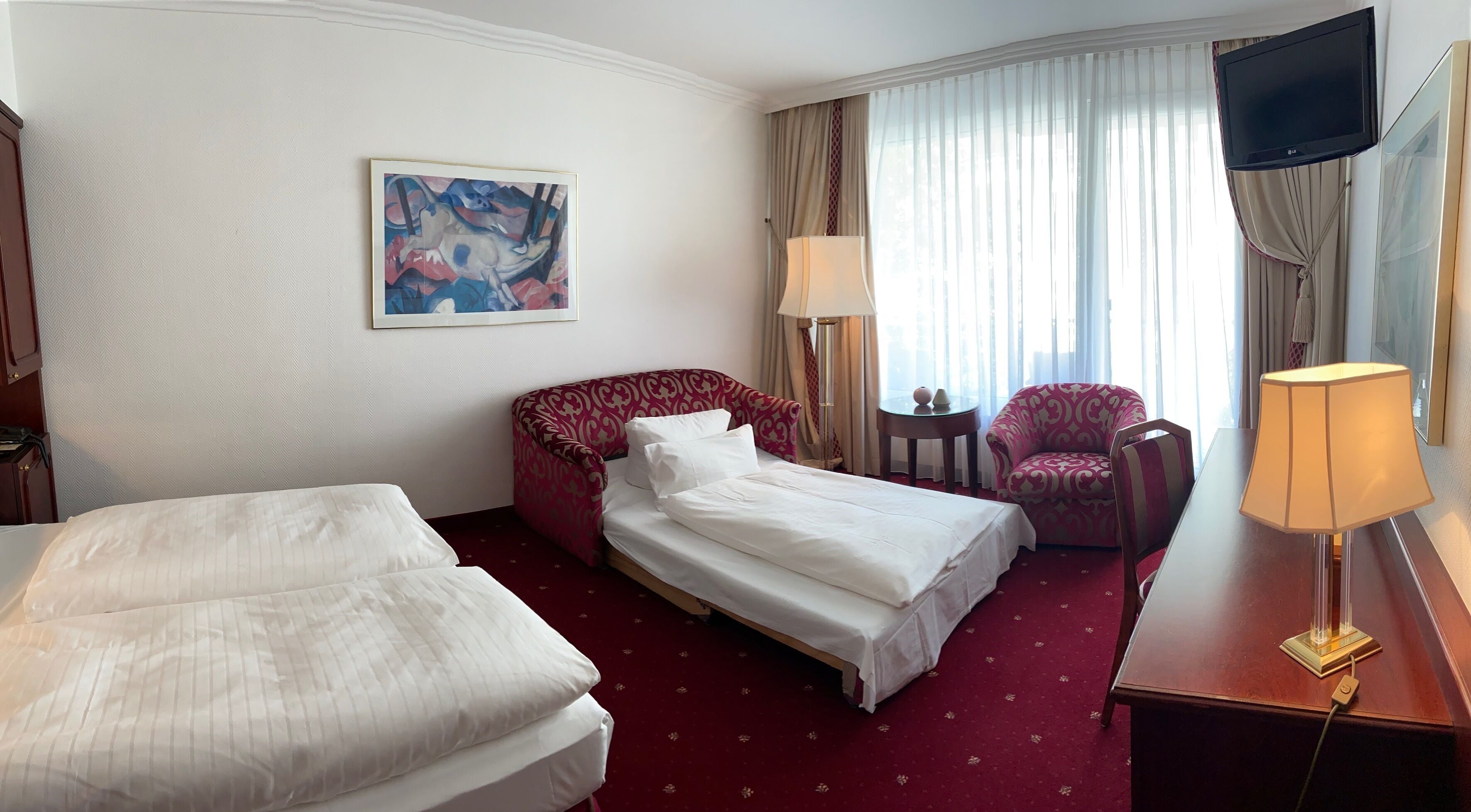 A hotel room with a bed, two bedside tables, a chair, a TV, and a painting on the wall.