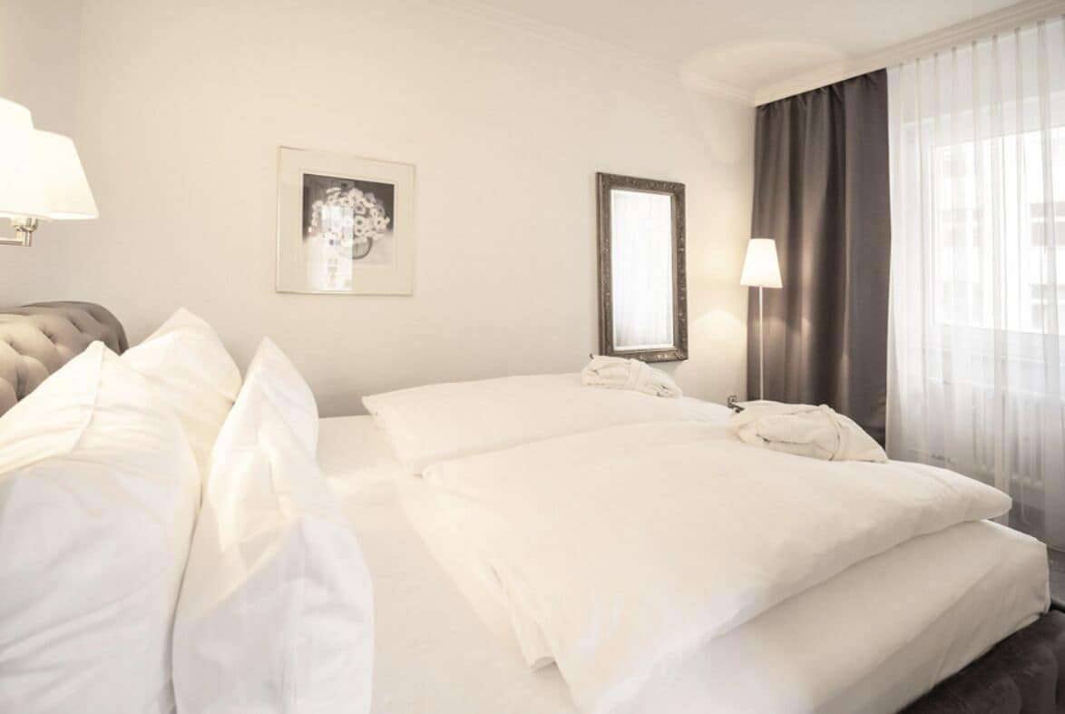A hotel room with a bed, a bedside table, a lamp, a framed picture, and a window with curtains.
