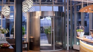A modern hotel lobby with a revolving door, a reception desk, and a glass wall offering a view of the street. - Kronenhotel Stuttgart (Stuttgart)