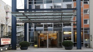 A modern hotel entrance with a glass canopy, a revolving door, and two potted plants. - Kronenhotel Stuttgart (Stuttgart)