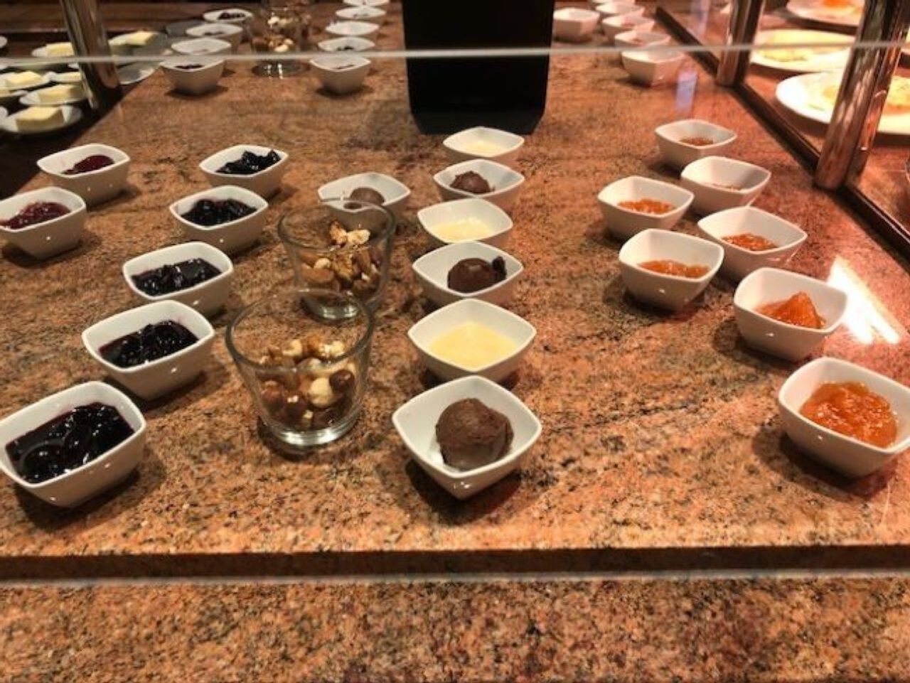 A buffet with various food items in small bowls, arranged on a granite countertop.