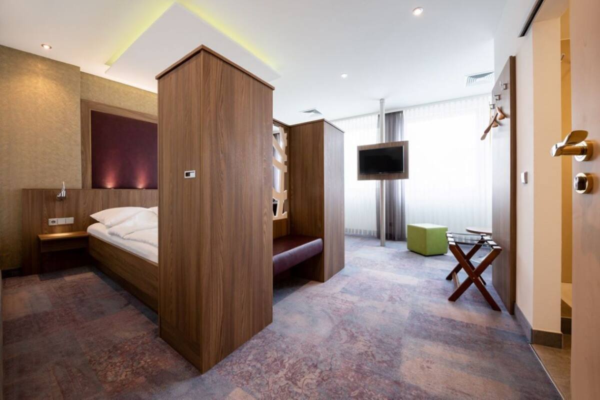 Une chambre d’hôtel moderne avec un lit en bois, un banc, une télévision et une petite table.