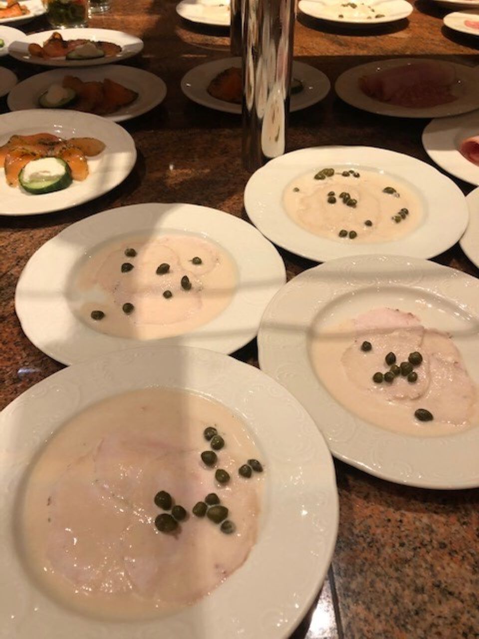 A dining table with plates of food, including a creamy dish with capers and slices of meat.
