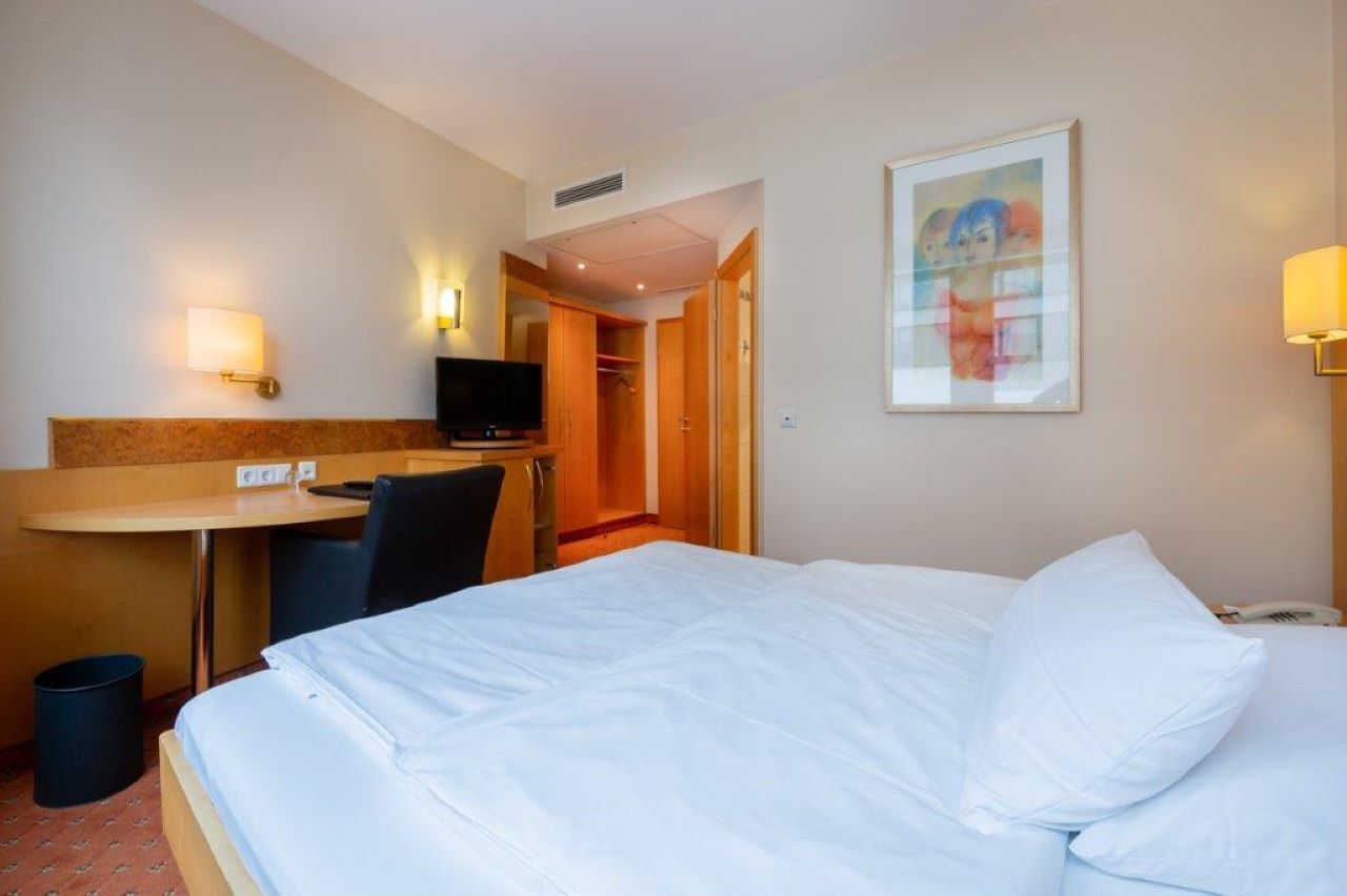 Een hotelkamer met een bed, een bureau, een stoel, een televisie en een schilderij aan de muur.