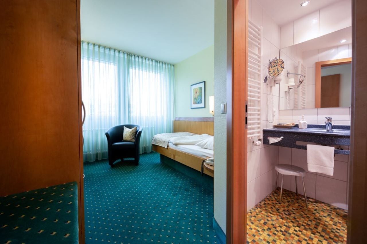A hotel room with a bed, a chair, a bathroom with a sink and mirror, and a patterned floor.