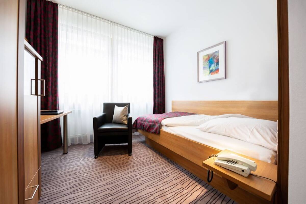 Une chambre d’hôtel avec un lit, un bureau, une chaise, un téléphone et un tableau au mur.