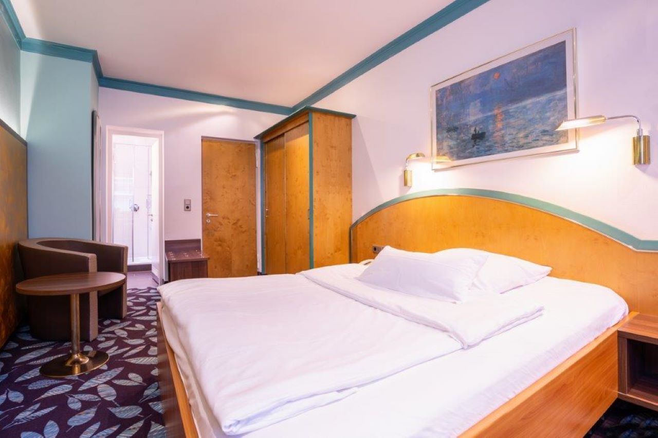 Una habitación de hotel con una cama, una silla, un escritorio y un cuadro en la pared.