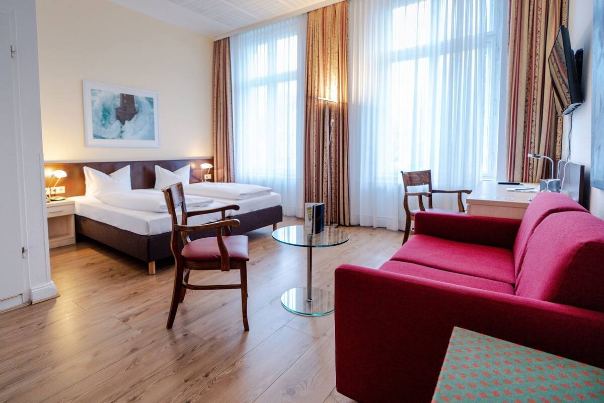 Ein Hotelzimmer mit einem Bett, einem roten Sofa, einem Glastisch und einem Sessel.