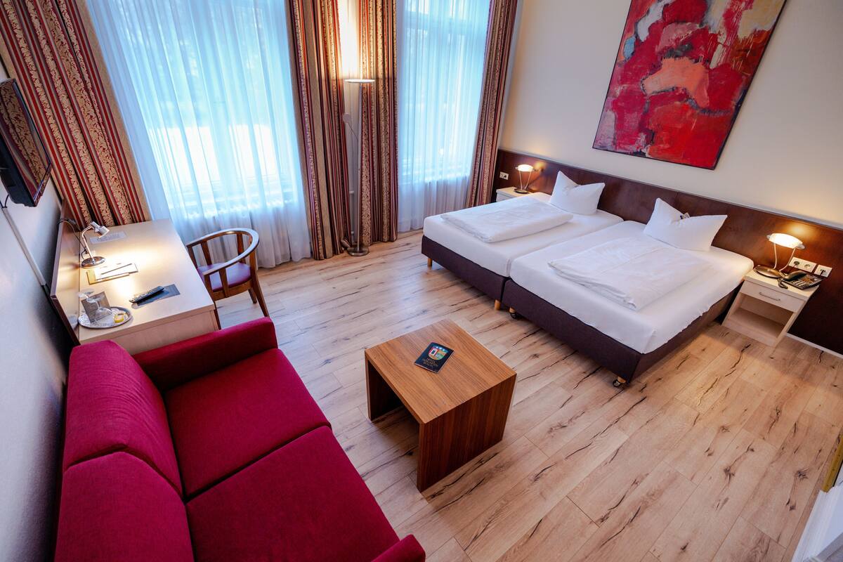 Ein Hotelzimmer mit einem Bett, einem roten Sofa, einem Holztisch und einer Lampe.