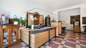 A reception desk with a wooden counter, a potted plant, and a mirror. There are chairs and a small bar area in the background. - Hotel Tiergarten Berlin (Berlin)