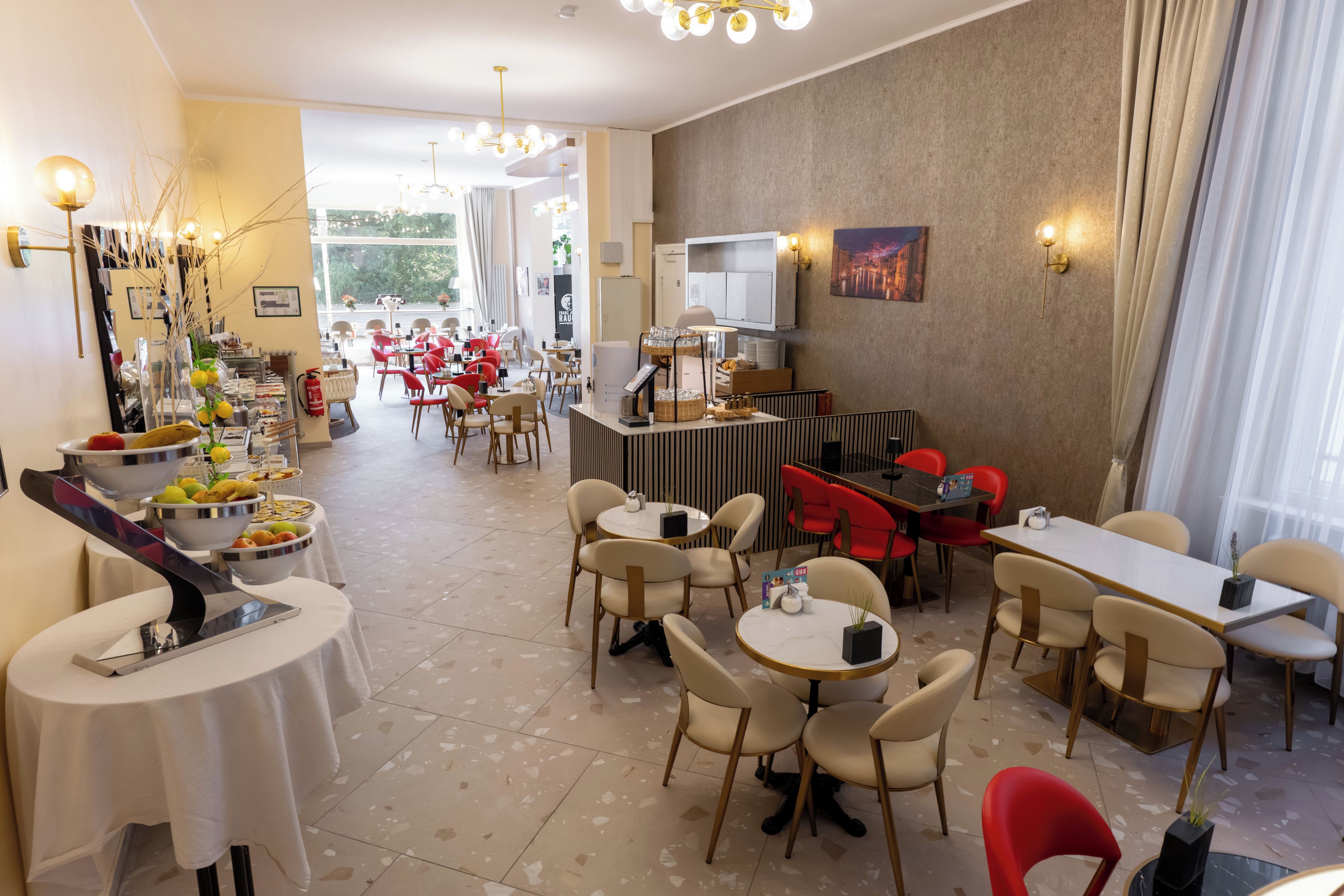 A hotel dining area with round tables and chairs, a buffet with fruits and pastries, and a view of the outdoors.