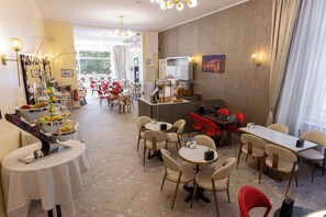 A hotel dining area with round tables and chairs, a buffet with fruits and pastries, and a view of the outdoors. - Hotel Tiergarten Berlin (Berlin)