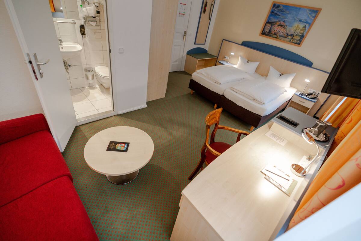 Ein Hotelzimmer mit Bett, Nachttisch, Stuhl und einem kleinen runden Tisch mit einem Buch.