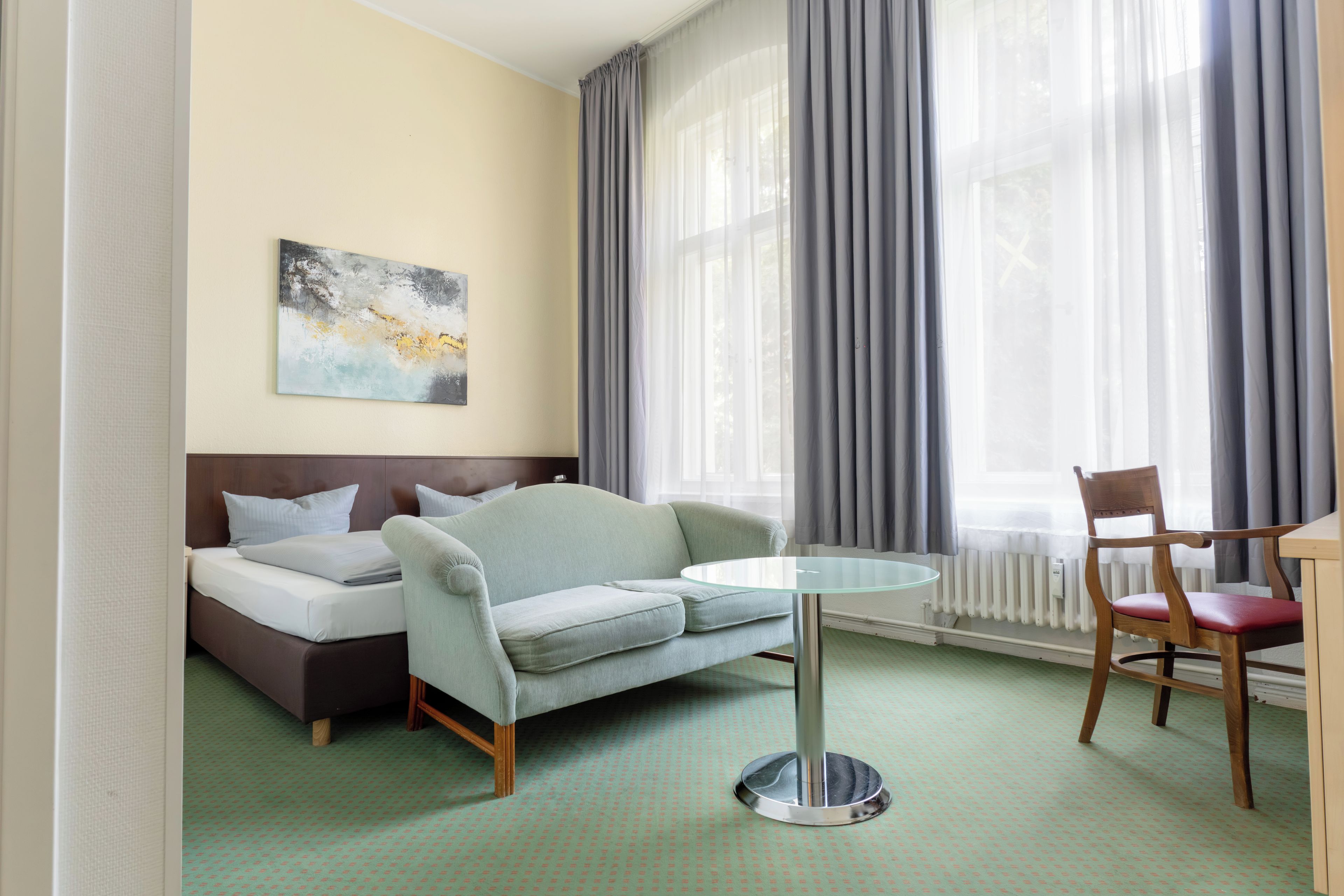 A hotel room with a bed, a sofa, a dining table, and a chair.