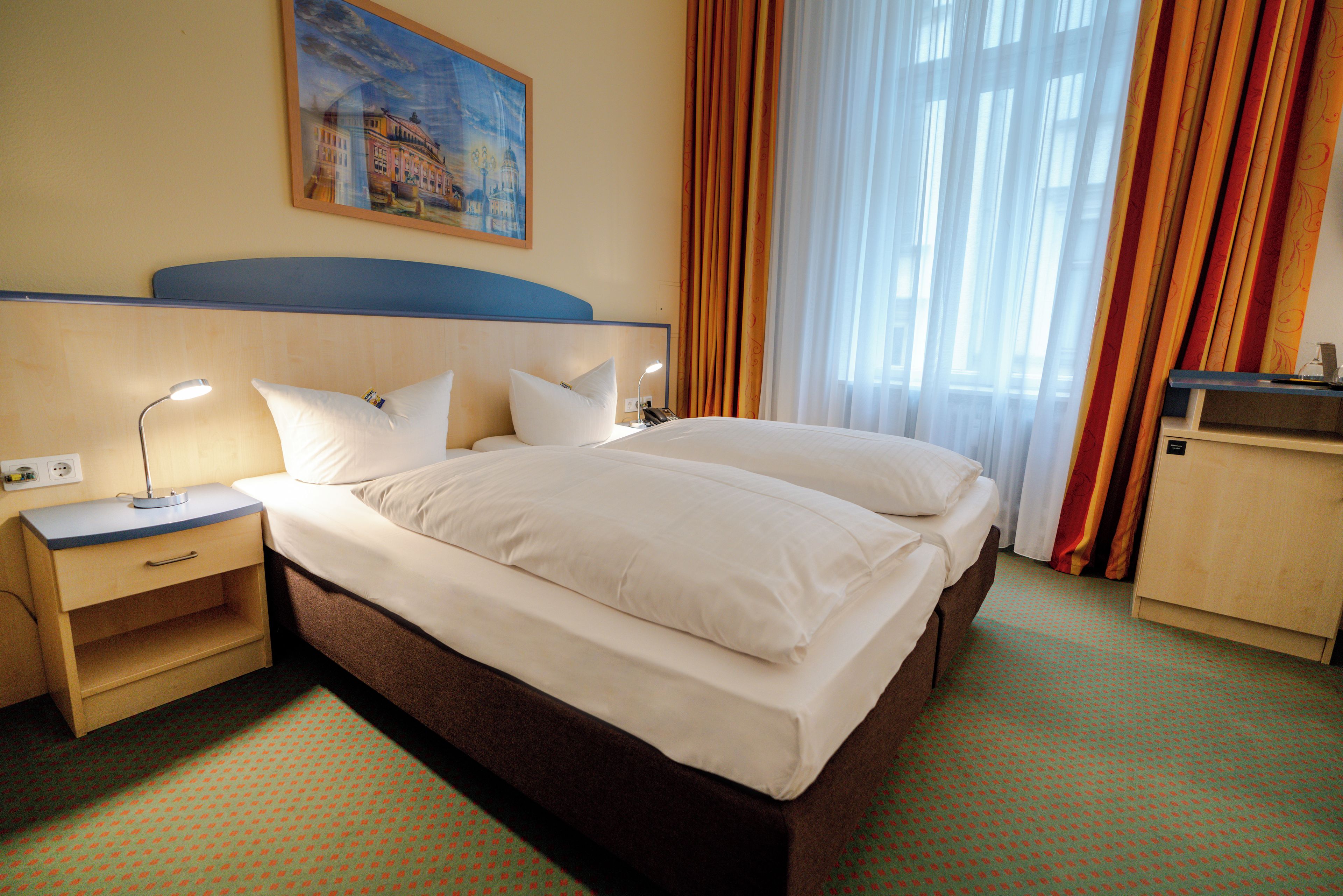 Una habitación de hotel con una cama, mesitas de noche, una lámpara y un cuadro en la pared.