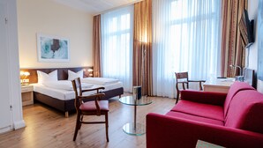 A hotel room with a bed, two chairs, a red sofa, a small table, and a TV.