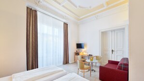 A hotel room with two beds, a desk with a chair, a television, and a red sofa. - Hotel Tiergarten Berlin (Berlin)
