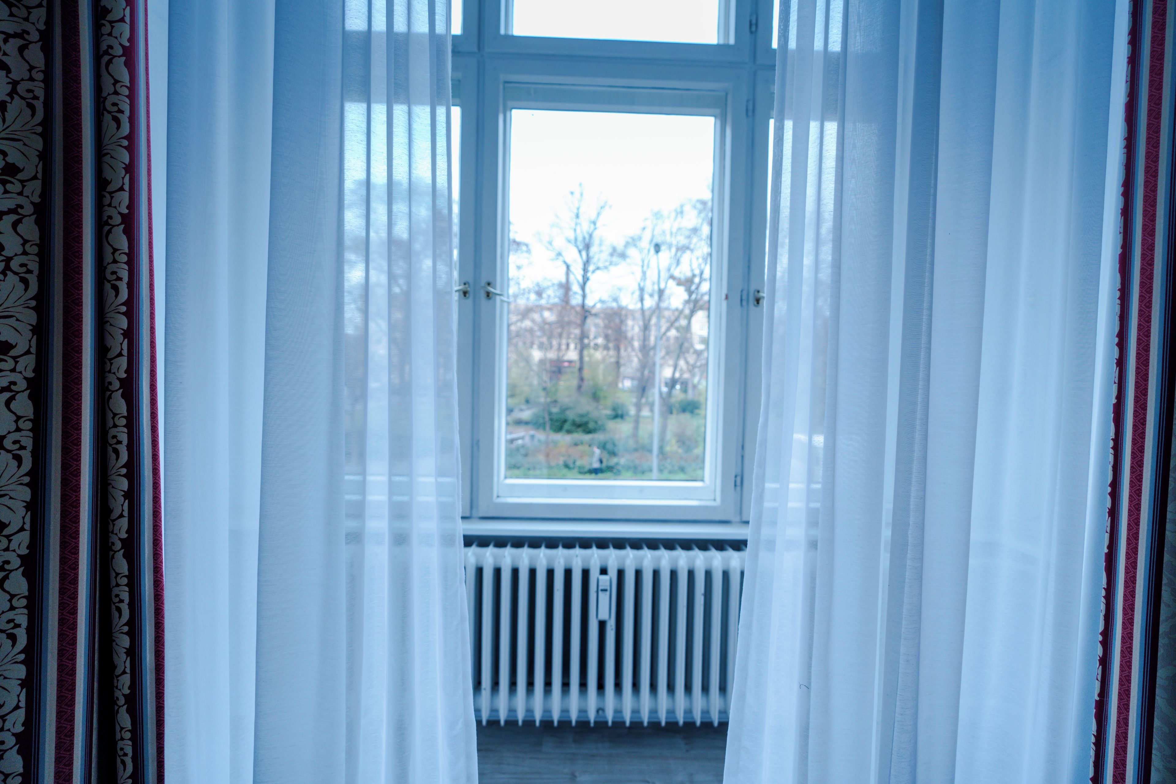 Ein Zimmer mit Fenster, Vorhängen und Heizkörper.