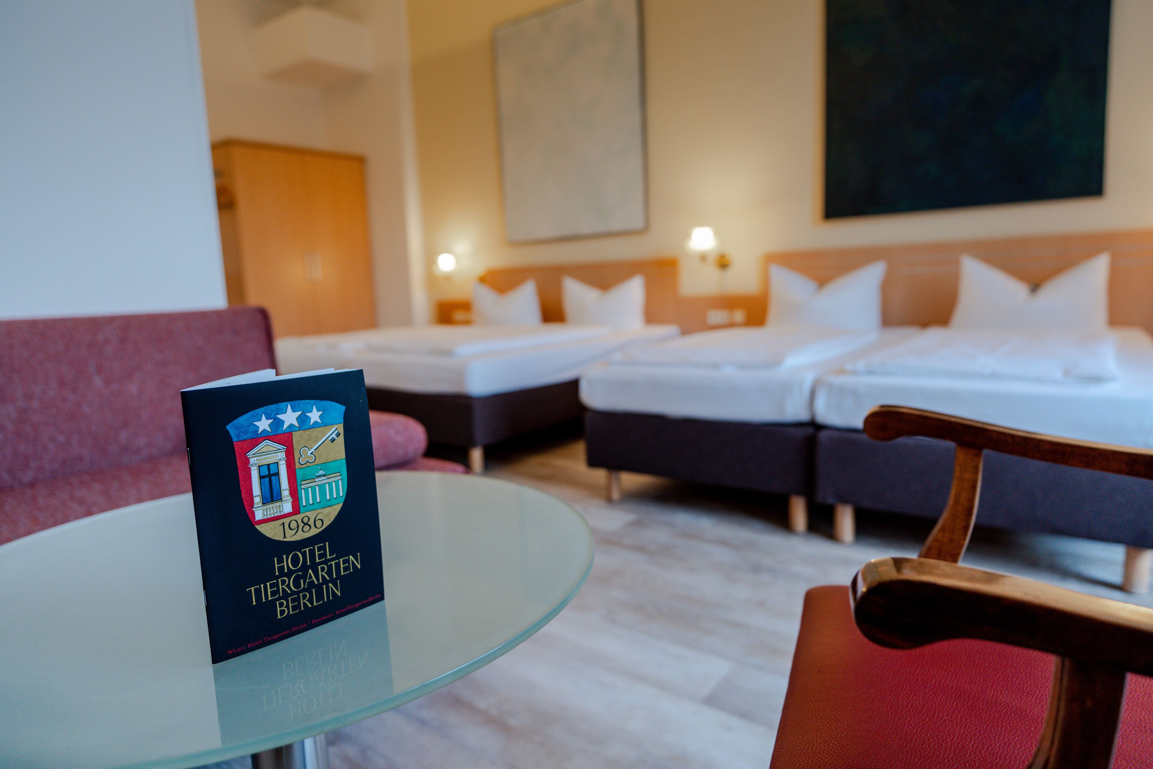 A hotel room with a glass table, a red chair, two beds, and a red sofa.