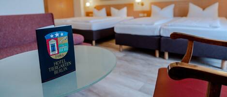 A hotel room with a glass table, a red chair, two beds, and a red sofa.