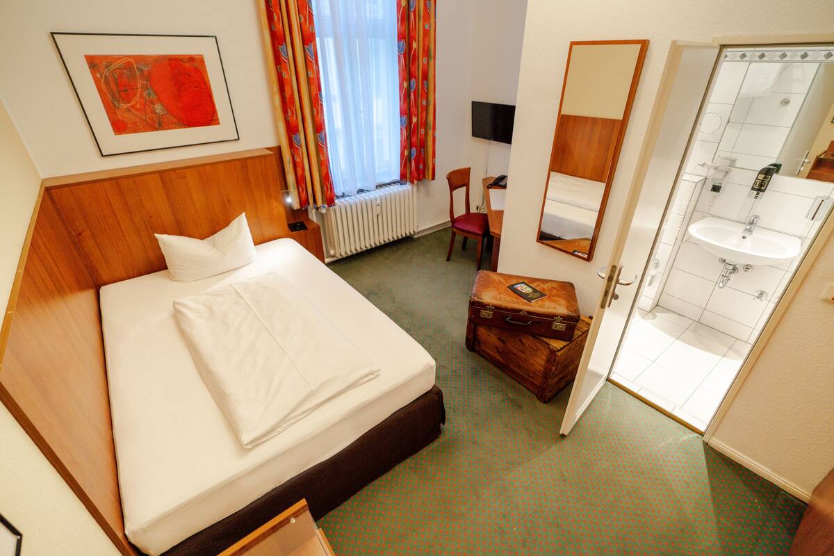 Ein Hotelzimmer mit einem Bett, einem Schreibtisch, einem Stuhl, einem Koffer, einem Fernseher und einem Badezimmer mit Waschbecken und Spiegel.