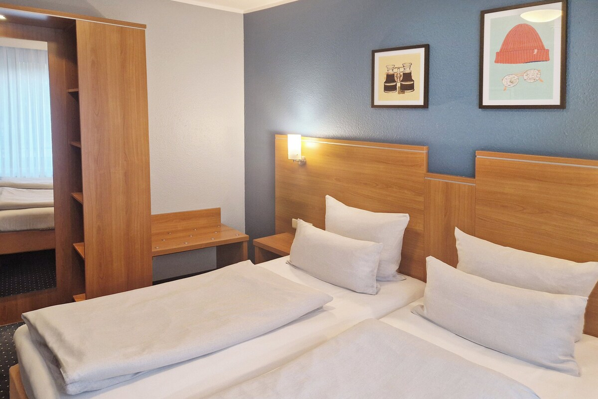 A hotel room with two beds, a wooden headboard, a nightstand, and a wardrobe.