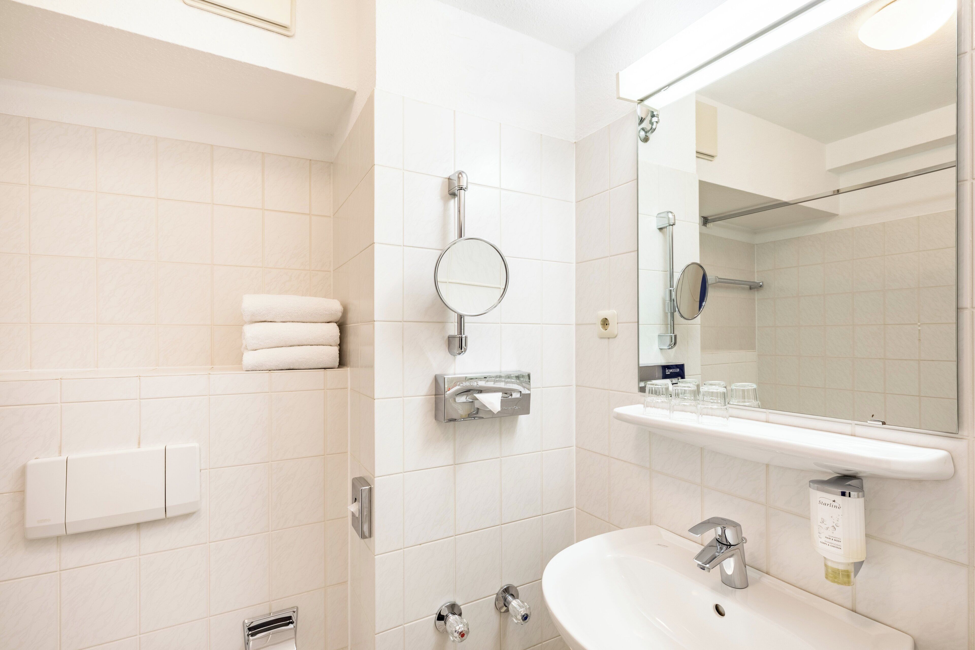 Un baño moderno con un lavamanos blanco, un espejo, un perchero y una zona de ducha.