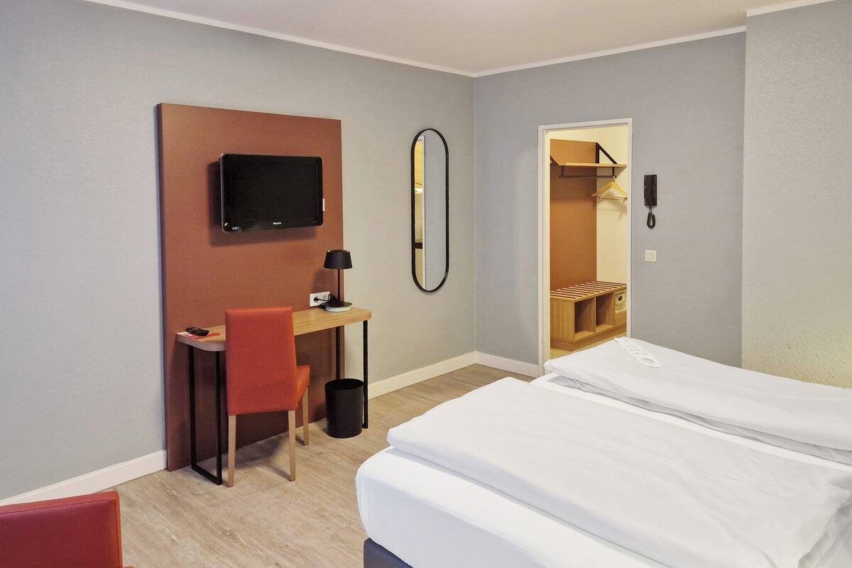 Een hotelkamer met een bed, een bureau, een stoel, een televisie, een spiegel en een telefoon.