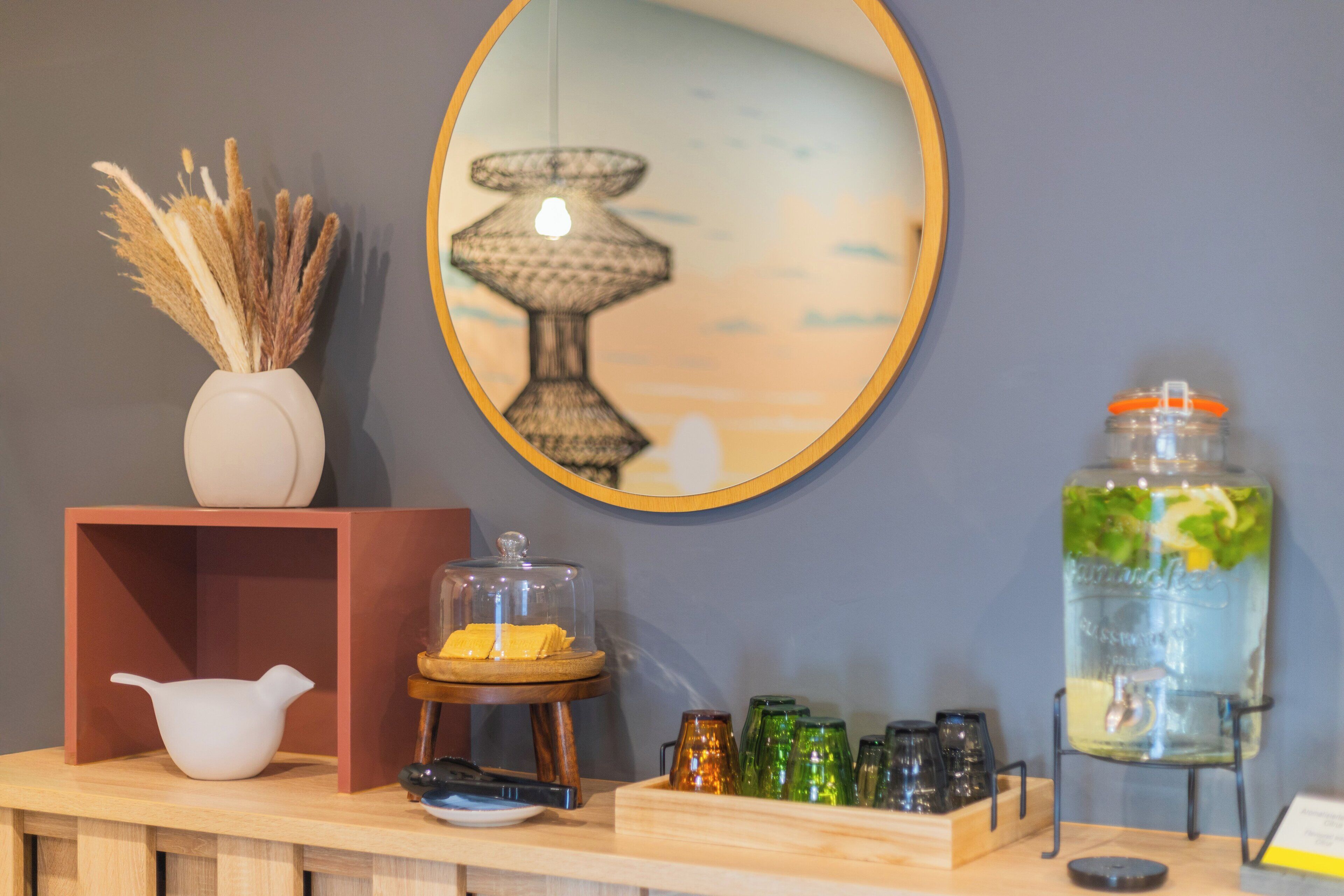 A wooden counter with a white vase, a glass jar with a lid, a small wooden stand, and a mirror on the wall.