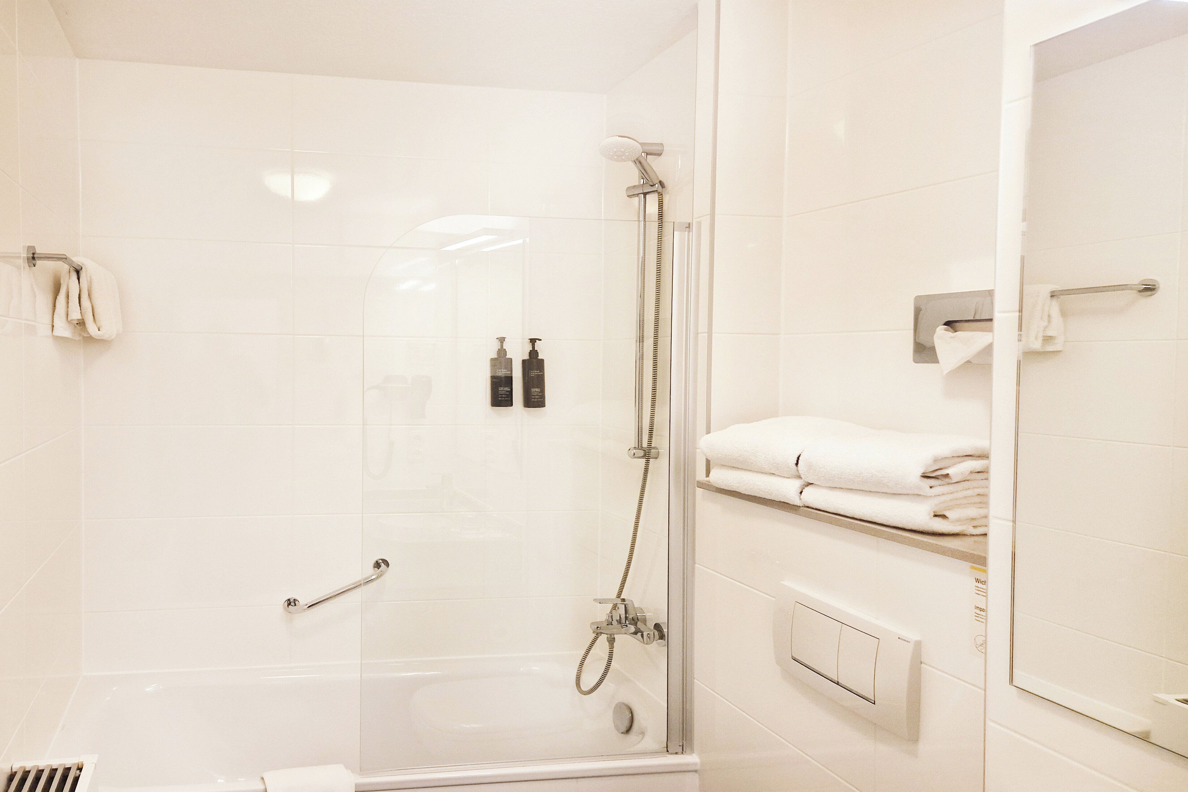 A modern bathroom with a glass-enclosed shower, a towel rack, and a built-in towel warmer.