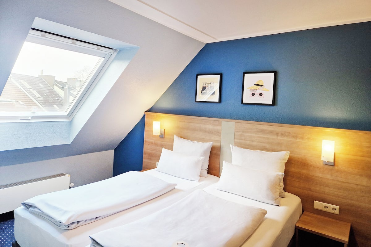 Een hotelkamer met dakraam, twee bedden, een houten hoofdeinde en twee wandlampen.