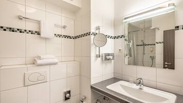 A modern bathroom with a large sink, a mirror, a towel rack, and a shower area.