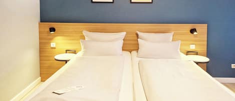 A double bed with white linens, two bedside tables with lamps, and two framed pictures on the wall.