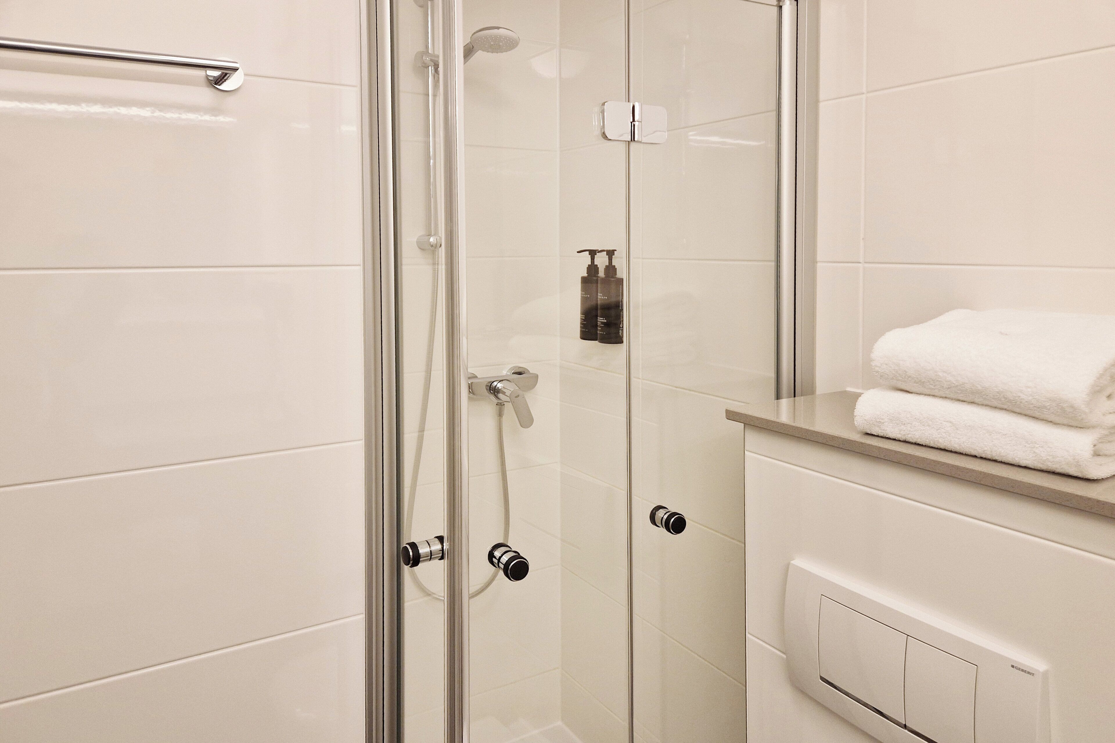 Une douche fermée par des parois de verre, dotée d’un panneau de commande, d’un porte-serviettes et d’un mur recouvert de carreaux blancs.