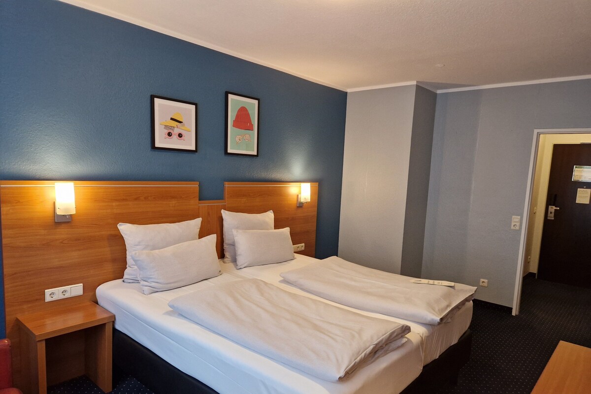 A hotel room with two beds, wooden headboards, white bedding, and two framed pictures on the wall.