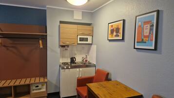 A compact kitchenette with a microwave, sink, and stove. There is a wooden table with two orange chairs and a bench with storage.
