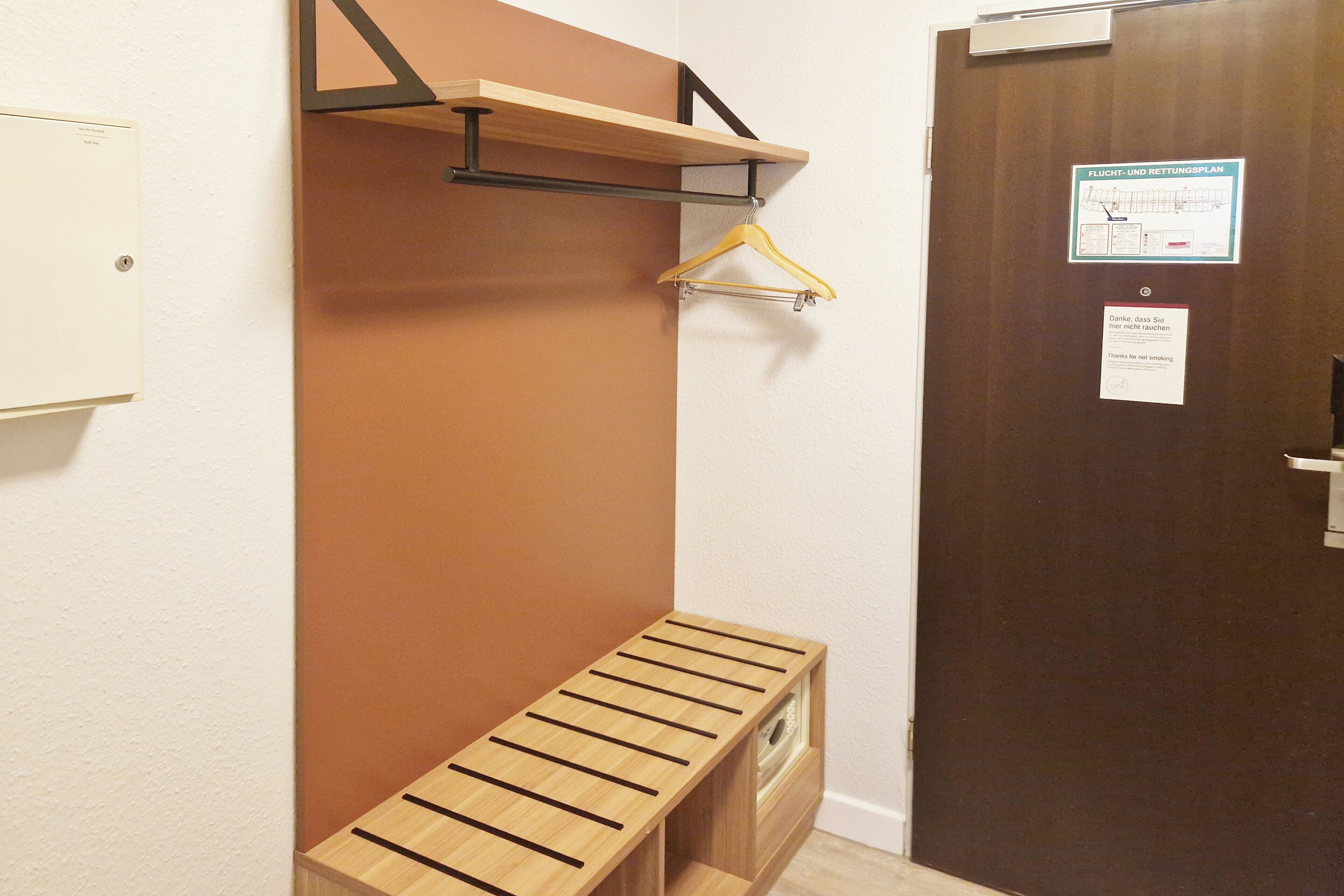 A room with a wooden bench, a coat rack, and a door with a sign.