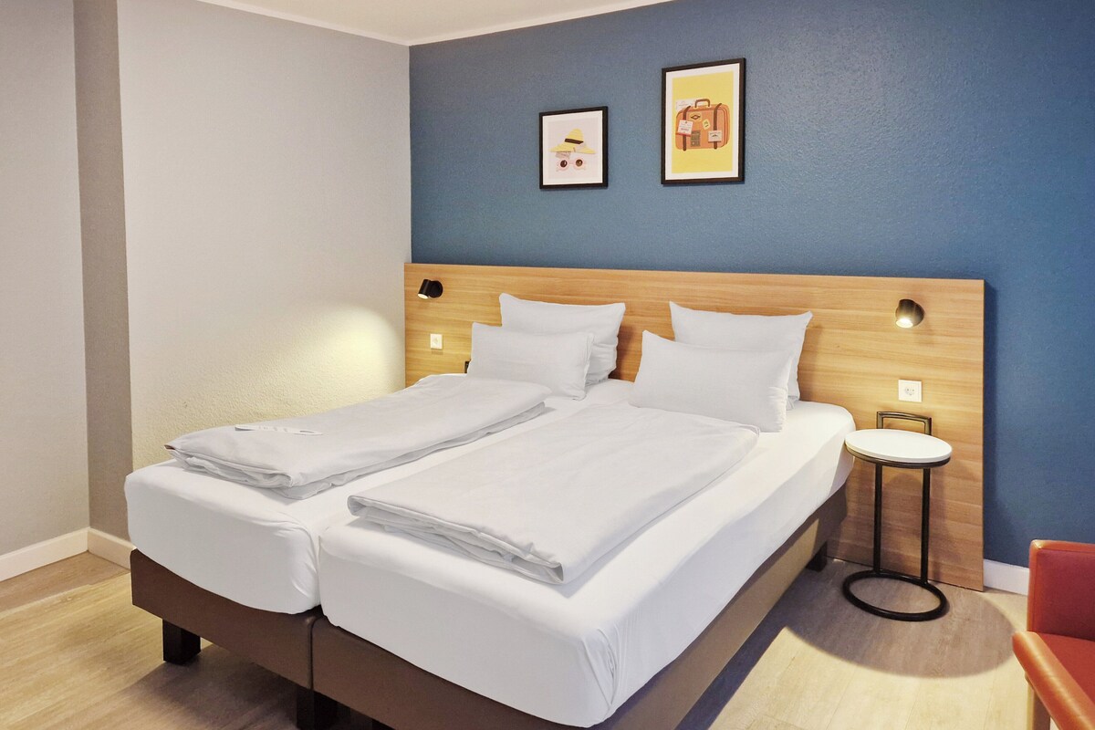 A double bed with white linens, a wooden headboard, and two wall-mounted lights.
