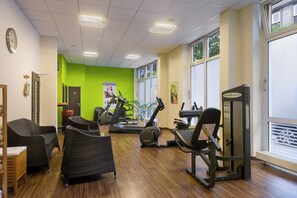 Een fitnessruimte met trainingsapparatuur, rieten stoelen en een groene accentmuur.