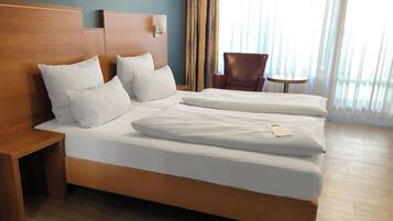 A hotel room with a double bed, a wooden headboard, a nightstand, a brown leather chair, and a small round table.