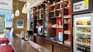 A modern bar area with a wooden counter, bar stools, and a refrigerated display case with beverages. - Garner Hotel Bochum by IHG (Bochum)