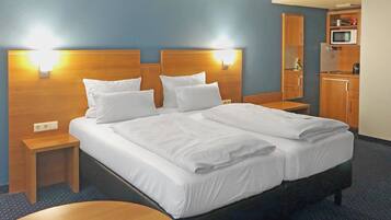 A hotel room with a large bed, two bedside tables, a round wooden table, a microwave, and a small kitchenette.
