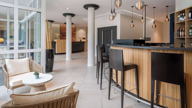 A modern bar area with high ceilings, pendant lighting, and a wooden bar counter. - Hotel Bochum Wattenscheid Affiliated by Meliá (Bochum)