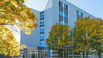 En moderne hotelbygning med glasfacade, tydelig indgang og parkeringsområde med træer.