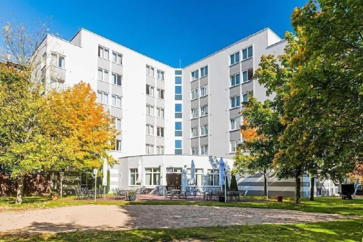 A multi-story building with a central courtyard, outdoor seating, and trees with autumn foliage.