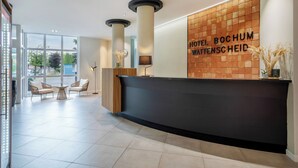 A hotel reception area with a modern design, featuring a reception desk, seating area, and a large window providing a view of the outdoors. - Hotel Bochum Wattenscheid Affiliated by Meliá (Bochum)