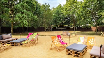 A backyard with a sandy area, wooden lounge chairs, and a volleyball net.