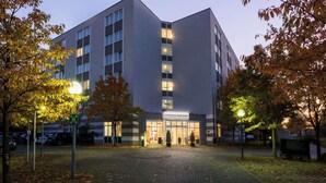 A modern hotel with a central entrance, surrounded by trees and a paved area. - Hotel Bochum Wattenscheid Affiliated by Meliá (Bochum)