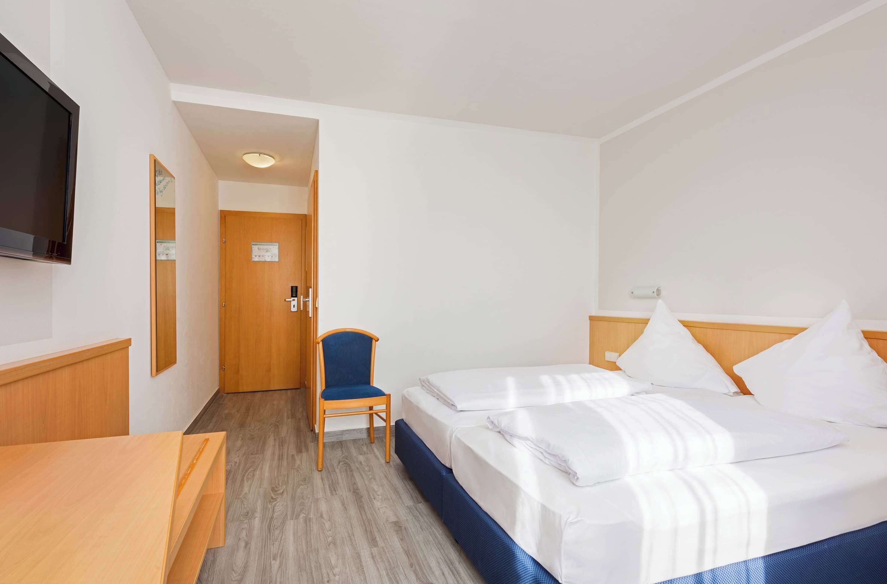 Een hotelkamer met twee bedden, een bureau, een stoel, een televisie en een deur naar een andere kamer.
