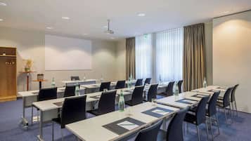 A conference room with tables, chairs, a projector screen, and a large window with curtains.